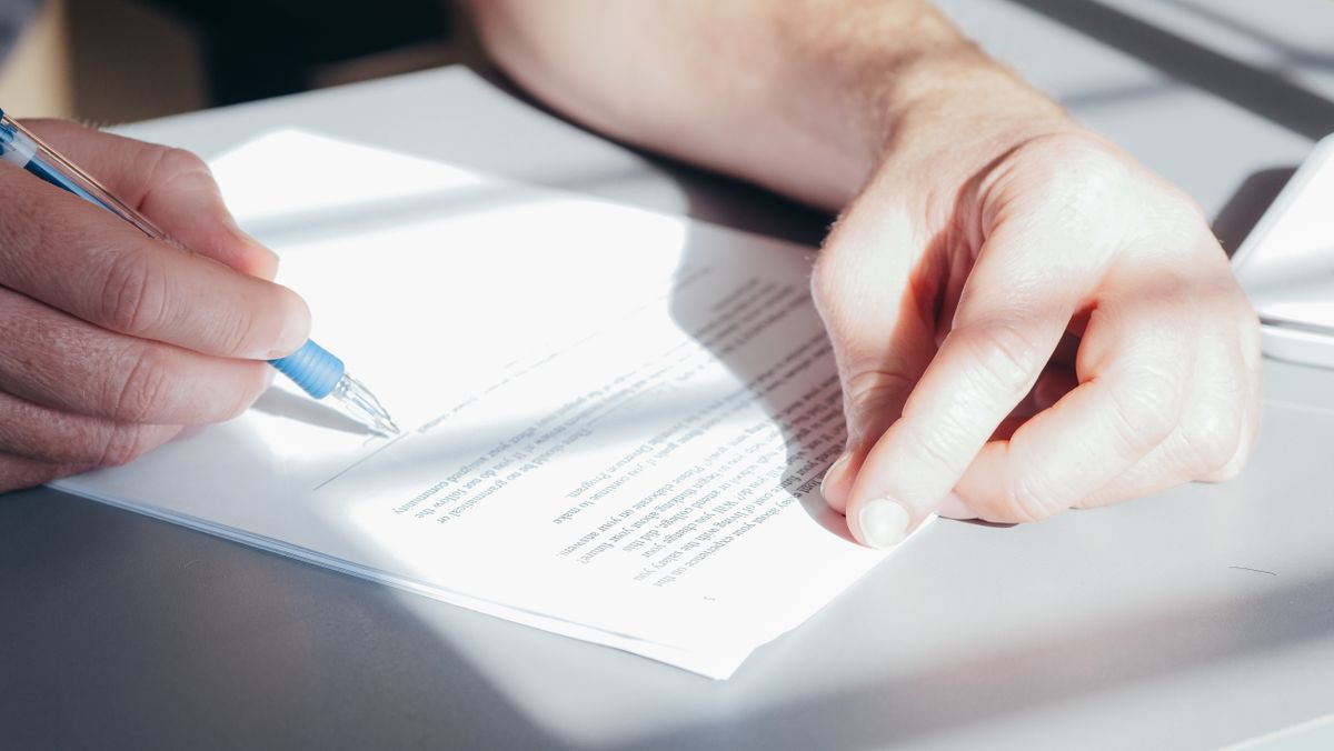 Mains signant un document contractuel avec un stylo sur un bureau clair