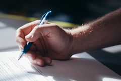 Detailed shot of a hand holding a blue pen while signing a document. Ideal for legal and business themes.