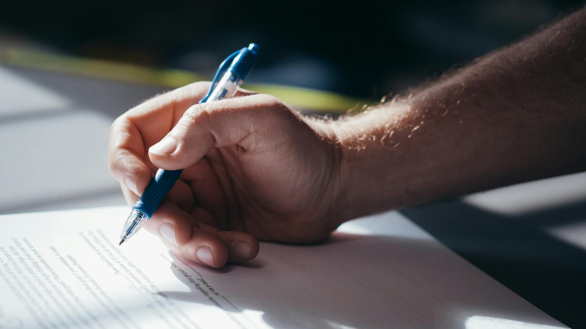 Detailed shot of a hand holding a blue pen while signing a document. Ideal for legal and business themes.