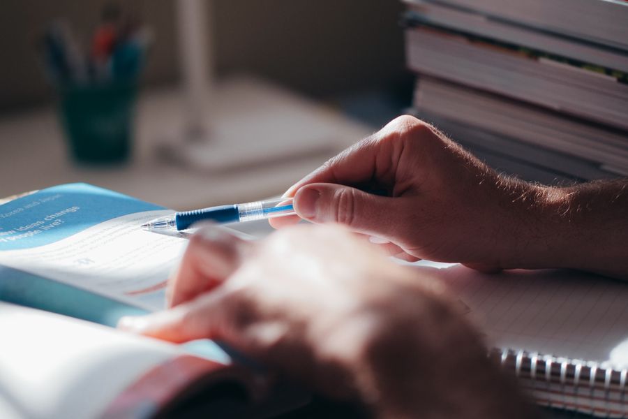 Close-up of hands writing in a notebook with a pen on a desk, suggesting focus and learning.