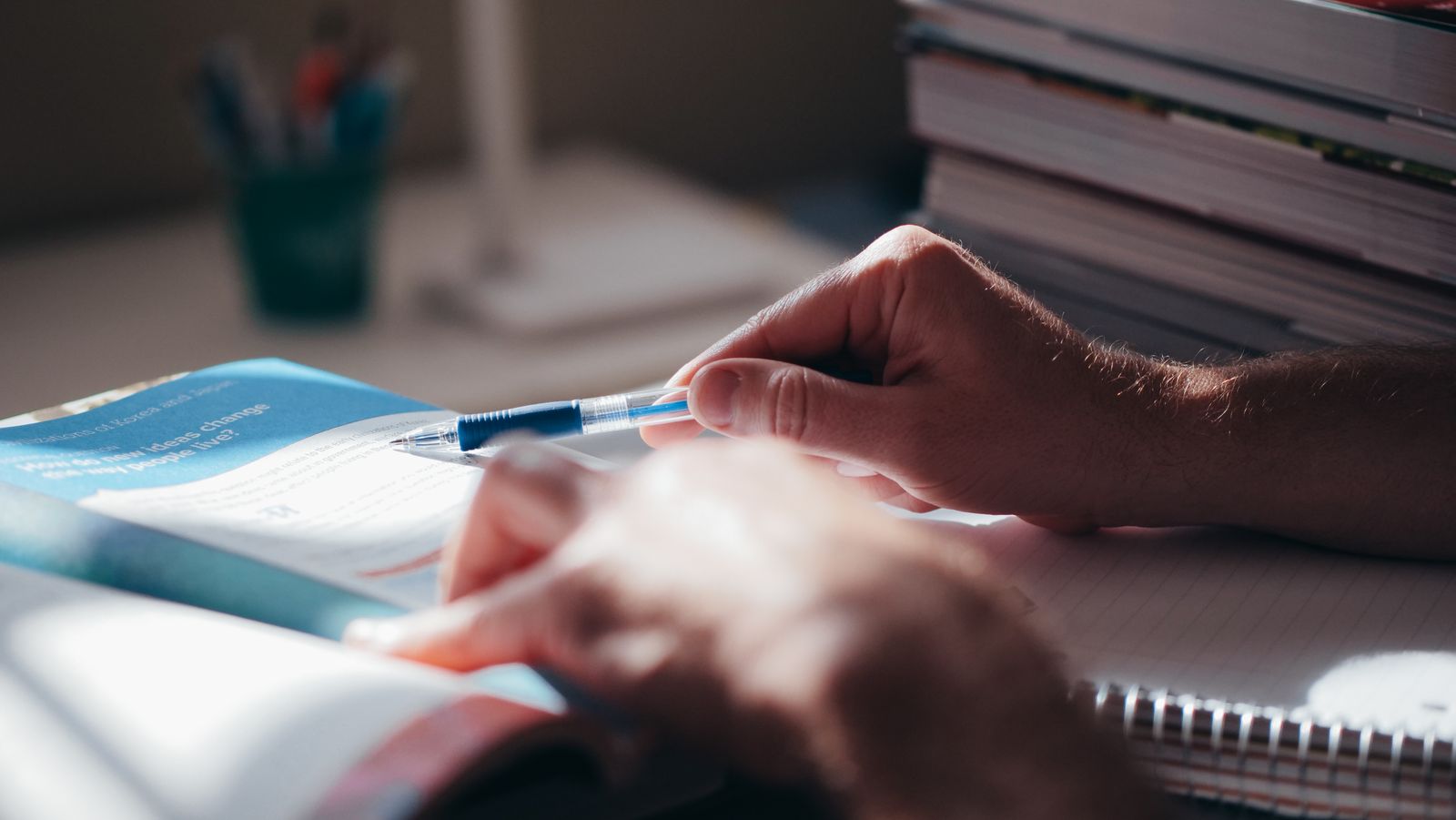 Hands writing notes with a pen beside an open book