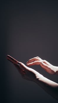 Close-up of hands holding a smartphone under dramatic lighting, highlighting modern technology use.