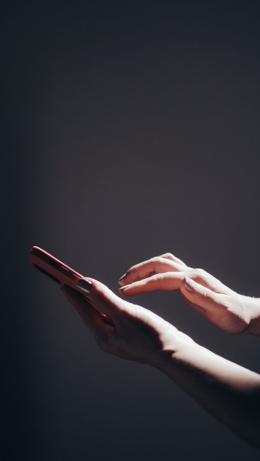 Hands tapping a smartphone under dramatic lighting — photo by Kindel Media on Pexels