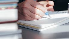Close-Up of a Person Writing on a Notebook