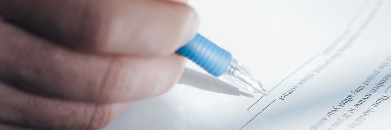 A close-up image showing a hand holding a pen while signing a document.