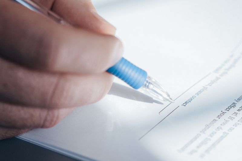 A close-up image showing a hand holding a pen while signing a document.