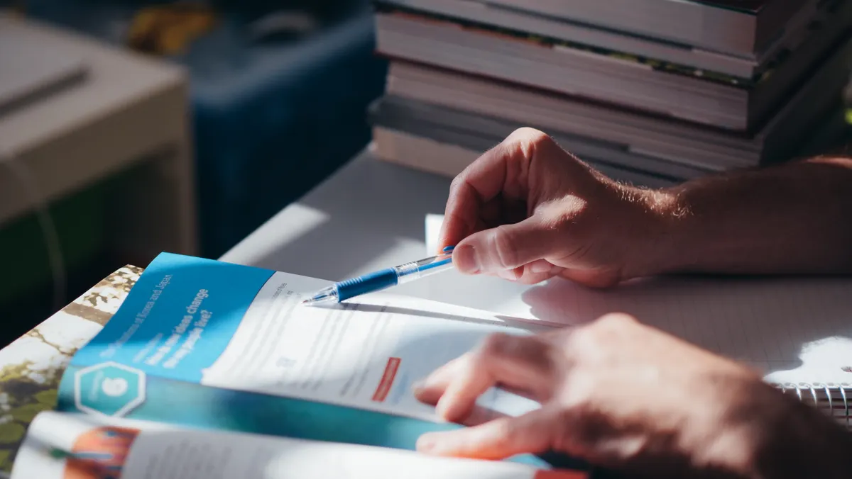 A hand holding a pen over a printed rulebook, representing a line-by-line check of Blue Guardian Futures rule changes.