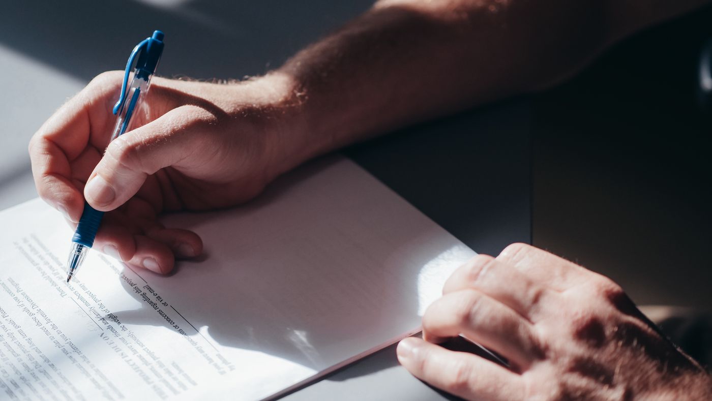 A hand signing a document with a blue pen in natural light