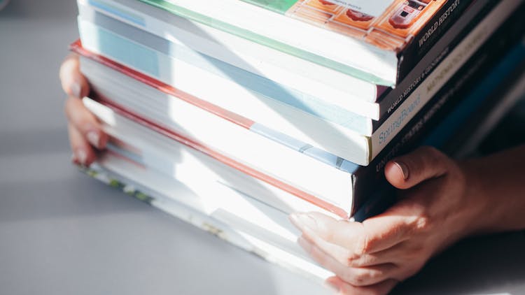 A Person Holding A Stack Of Books