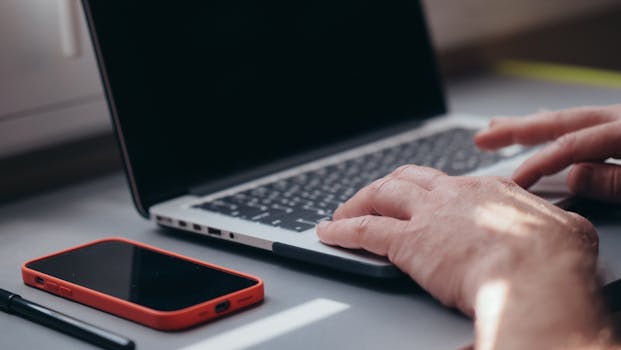 Close-up of hands typing on a laptop beside a smartphone. Ideal for tech and work themes.