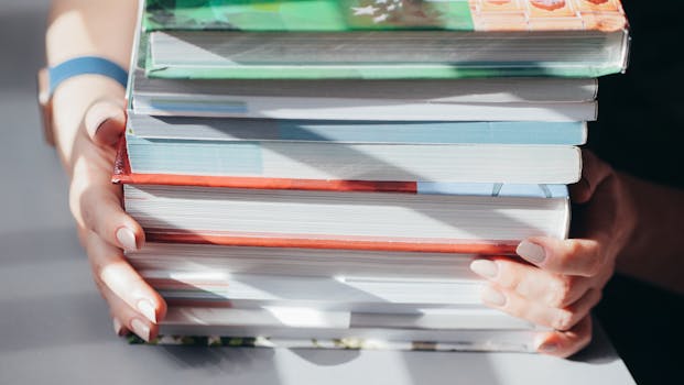 Close-up image showing hands holding a stack of colorful books under shaded light.