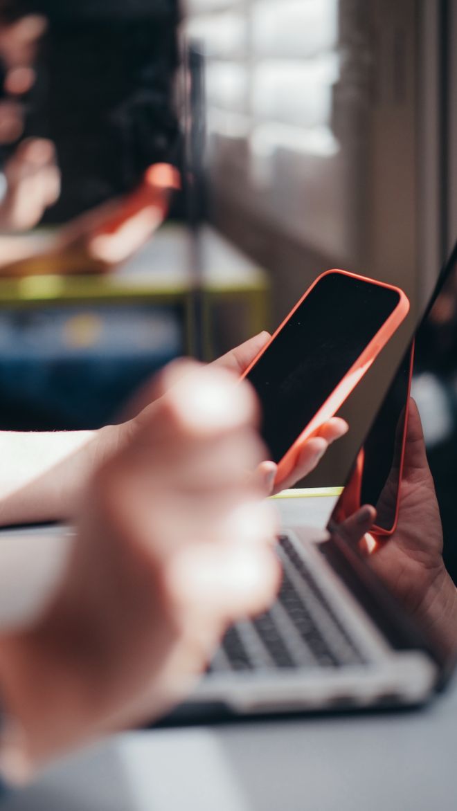 Hands holding a phone beside a laptop — photo by Kindel Media on Pexels