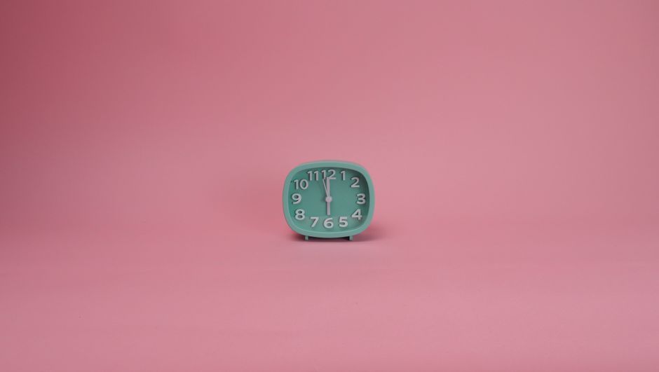 A minimalist mint green analog clock placed on a vibrant pink background.
