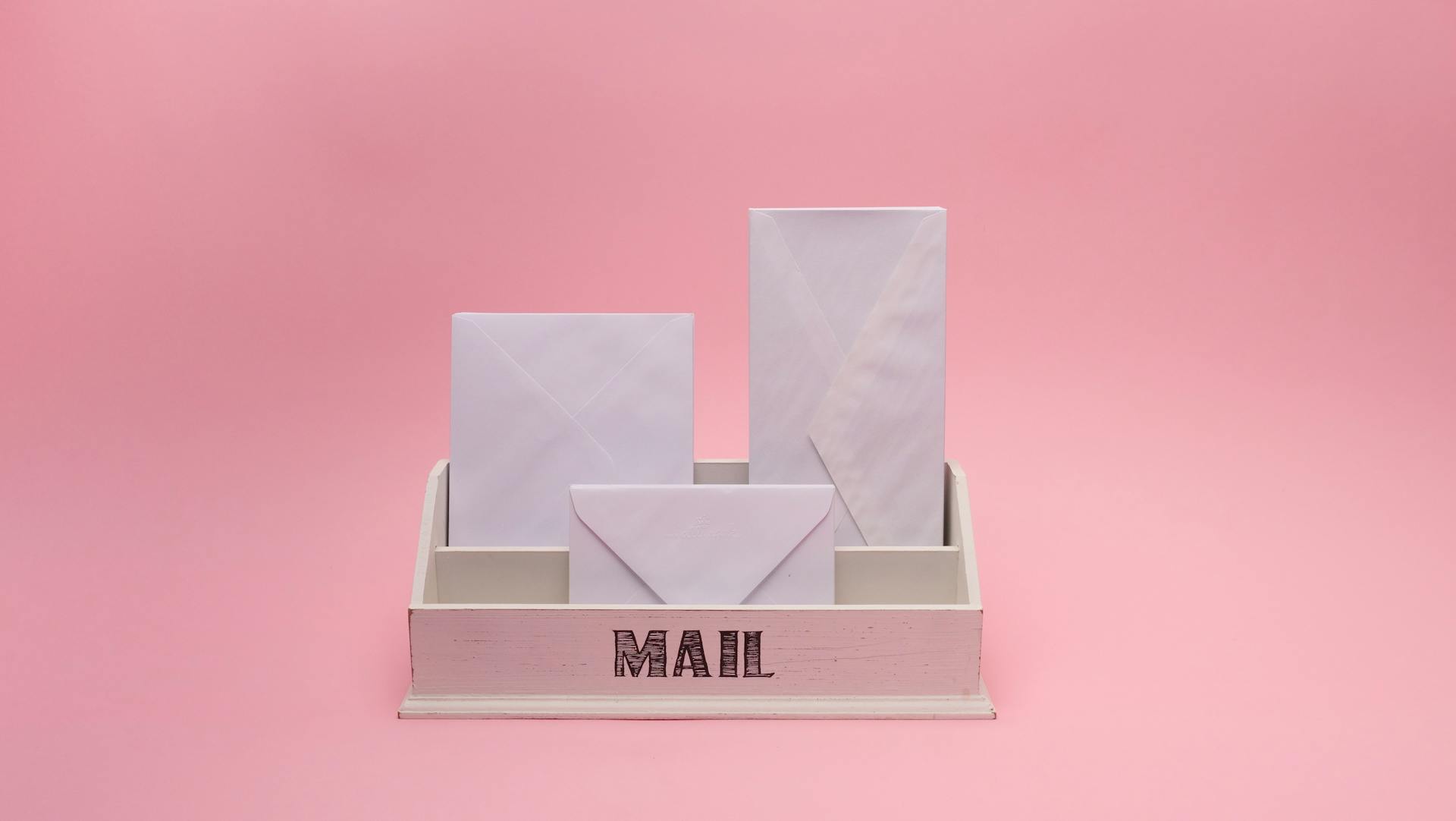 A minimalist white mail organizer with envelopes against a pink background, offering space for text.