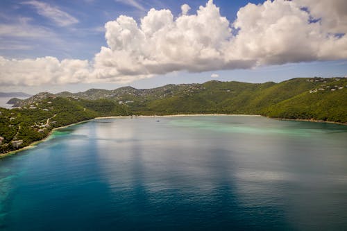 Body of Water Surrounded by Green Mountains Under White Clouds