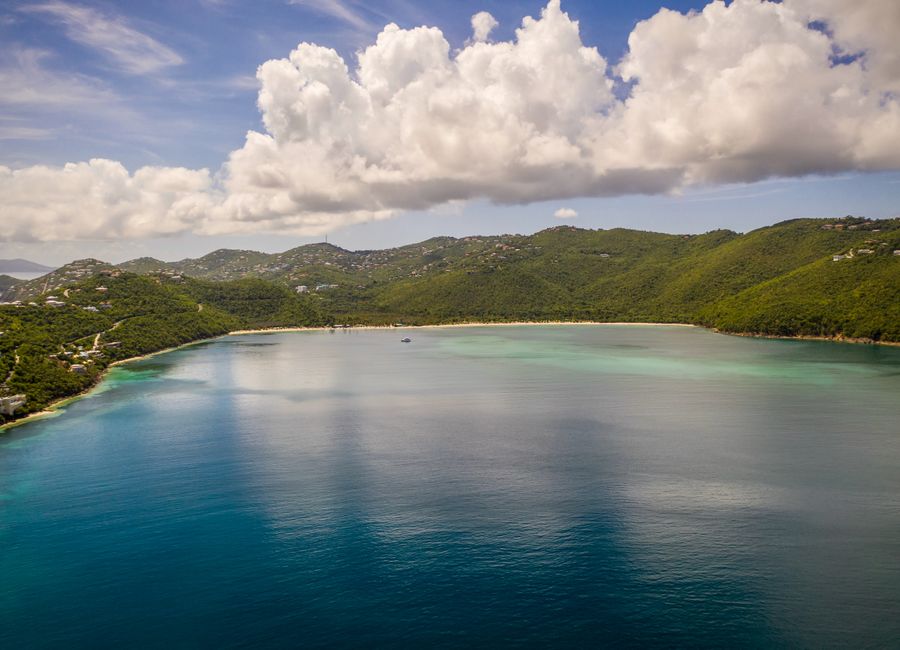 Scenic aerial view of St Thomas coastline with green mountains, clear blue sea, and fluffy clouds.