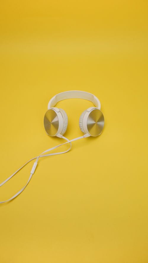 Free White headphones with sleek design on a bright yellow surface, perfect for tech visuals. Stock Photo