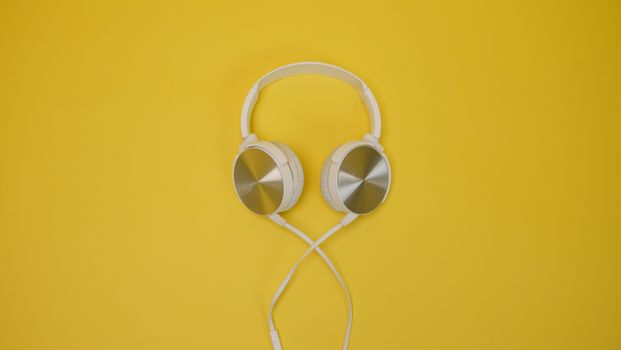 White and silver headphones displayed against a bright yellow backdrop, showcasing sleek design.