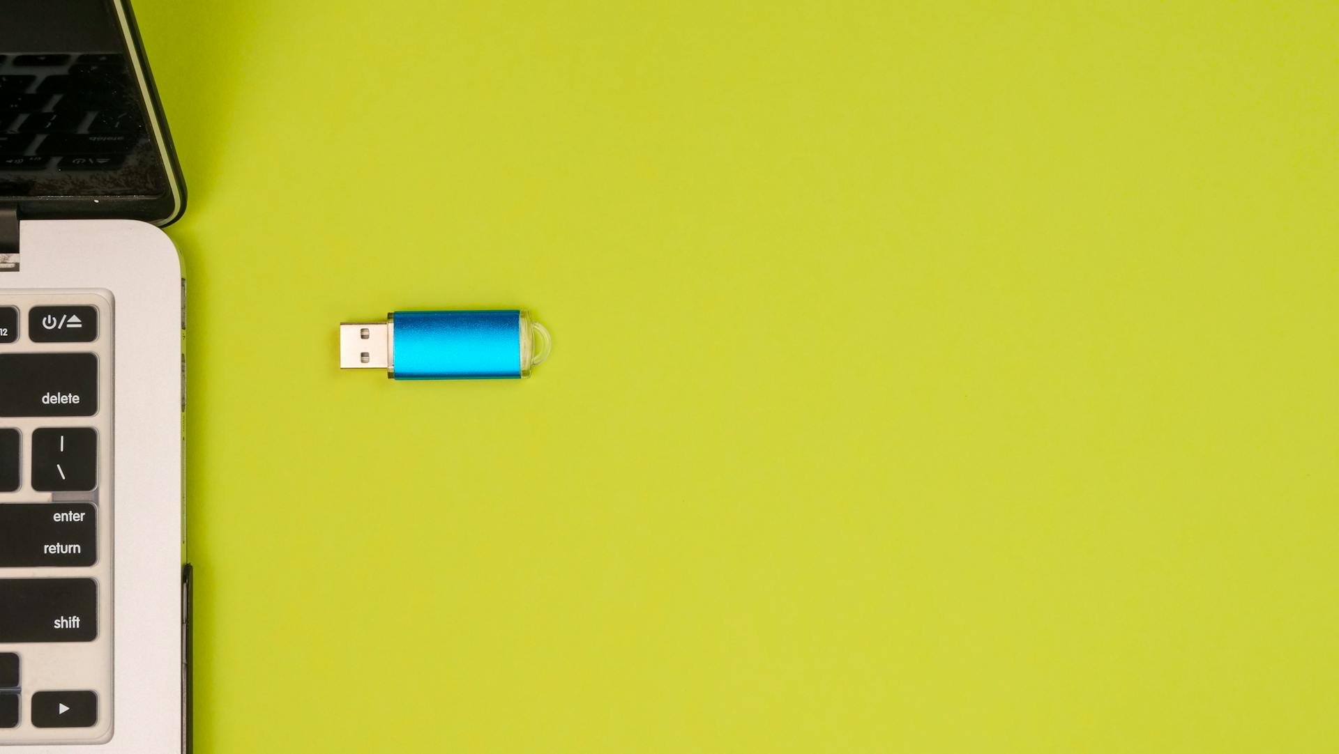 A blue USB drive next to a laptop on a vibrant yellow background, showcasing portable technology.