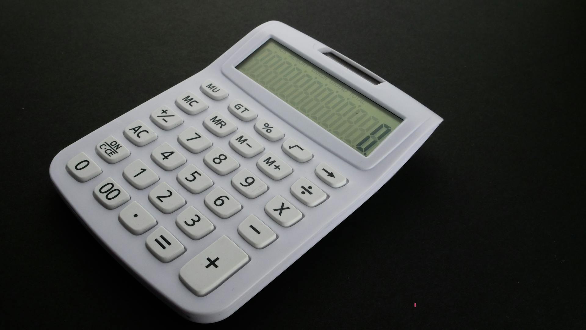 Close-up of a white calculator with a digital display on a black background.