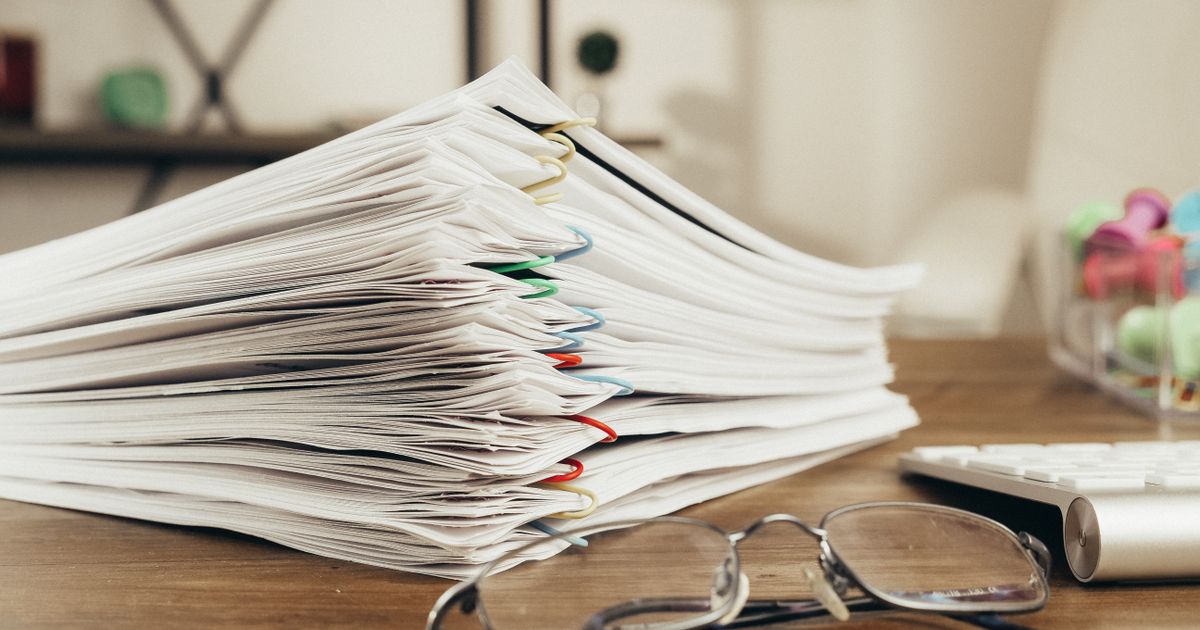 Gros plan sur une pile de documents de bureau tenus par des trombones, posée sur un bureau à côté d'une paire de lunettes.