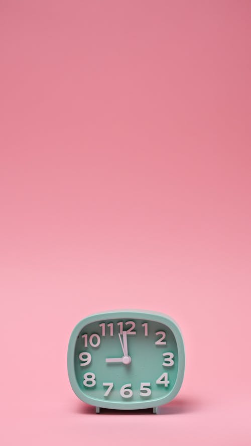 A Clock with White Hands on Pink Background