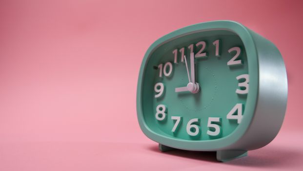 A green analog clock sits against a pastel pink background, showcasing a vibrant contrast.