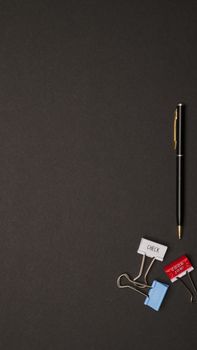 Minimalist overhead shot of a pen and assorted binder clips on a black surface.