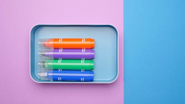 Four vibrant highlighters arranged neatly in a tray on a pastel pink and blue background.