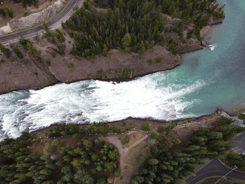 Free A breathtaking aerial view capturing a river cascading through lush green forests with rocky edges. Stock Photo