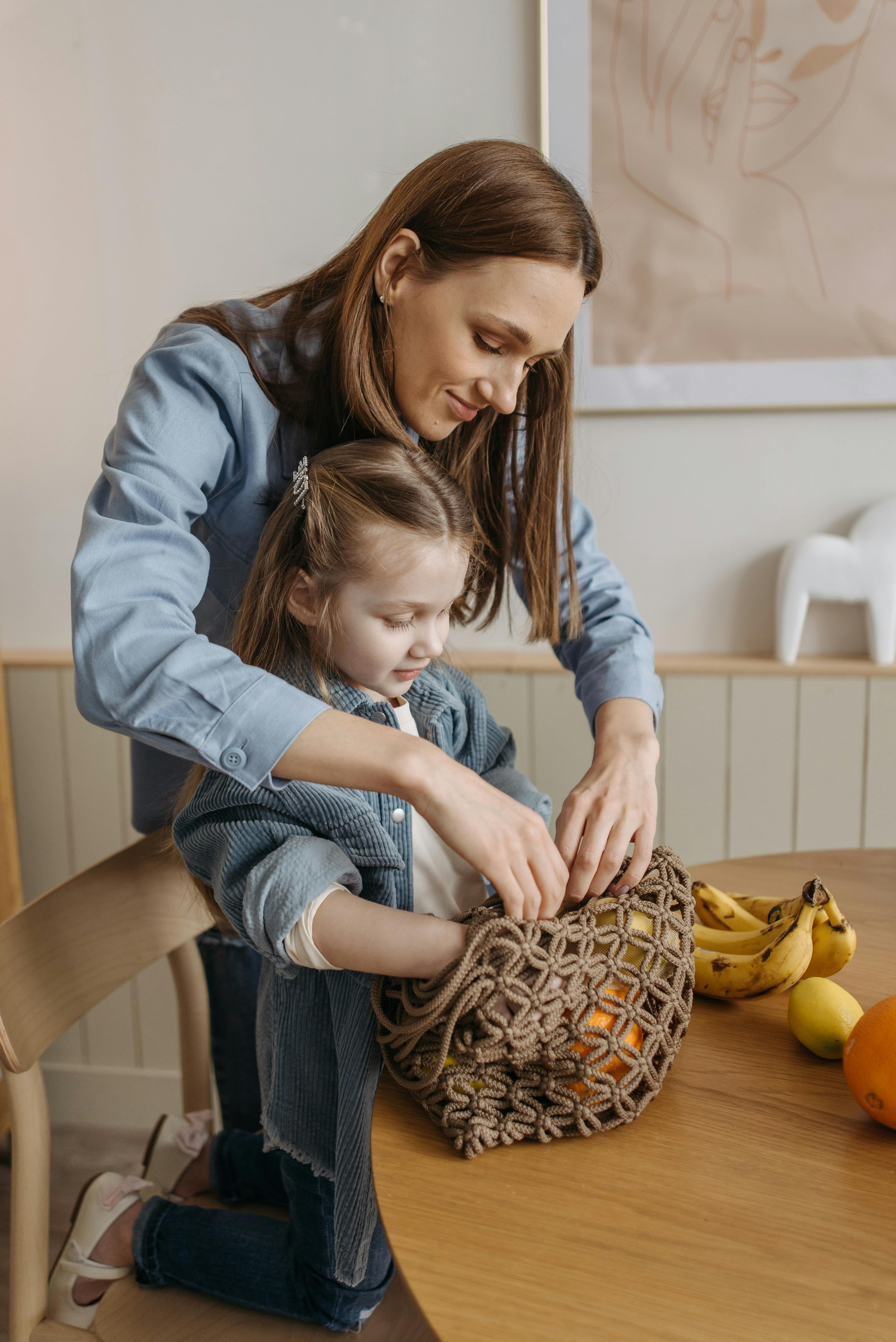 photo of a mother and her daughter getting fruits from a mesh bag