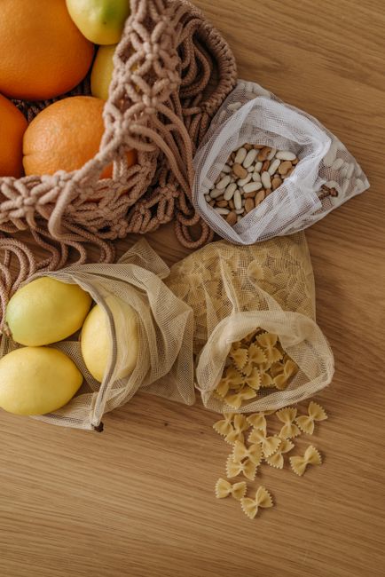 Overhead view of eco-friendly mesh bags with oranges, lemons, beans, and pasta on a wooden surface. - Pairing Dry Fruits with Honey and Shilajit for Health Benefits