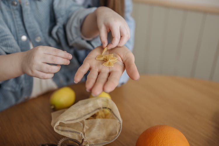 Hands Of A Child Placing Pasta On A Woman's Palm