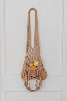 A sustainable mesh bag filled with various fruits hanging on a white door, promoting eco-friendly lifestyle.