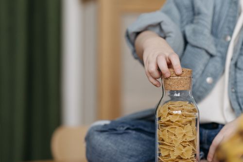 Free Close-up of a child holding a corked jar filled with uncooked bowtie pasta. Stock Photo