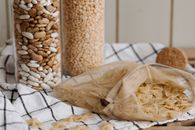 Spilled Uncooked Pasta in a Mesh Bag Near Beans in a Glass Container
