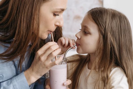 A mother and daughter sharing a strawberry milkshake indoors, depicting love and bonding.