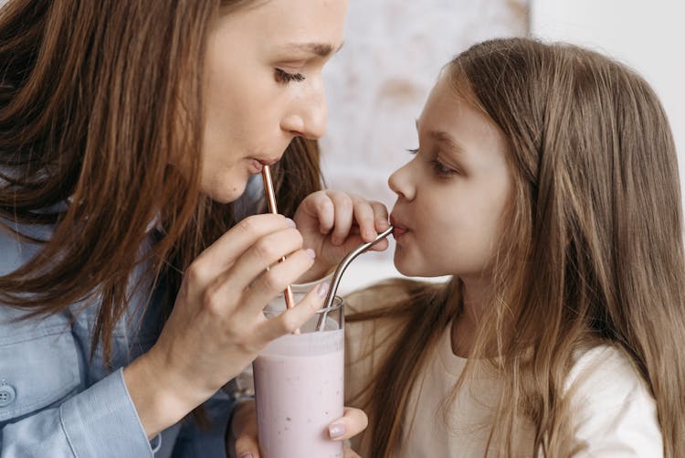 Woman And Child Sharing A Glass Of Milk Shake