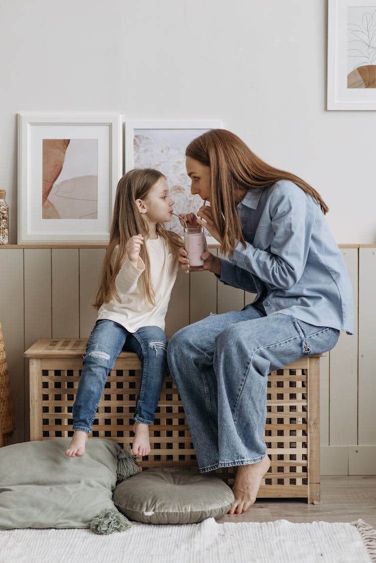 Woman And Child Sitting On A Wooden Bench While Sharing A Glass Of Milkshake