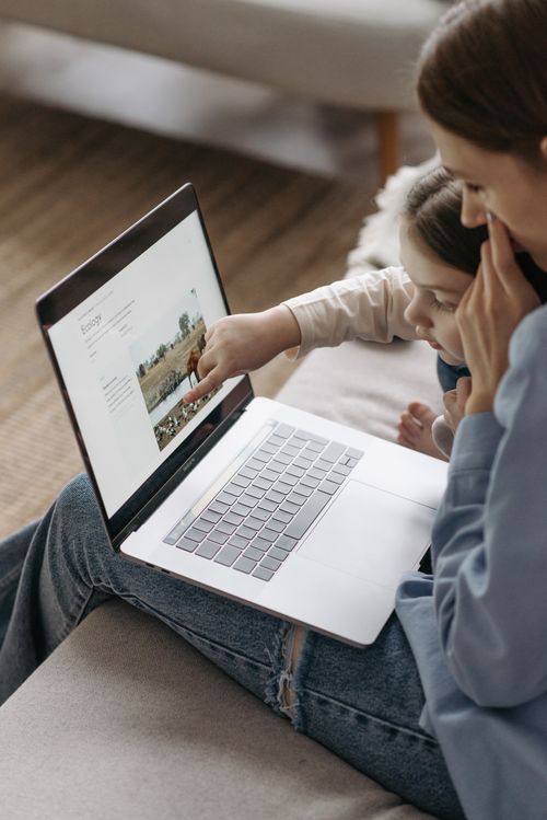 Free A mother and child sit together on a couch while exploring content on a laptop. Stock Photo