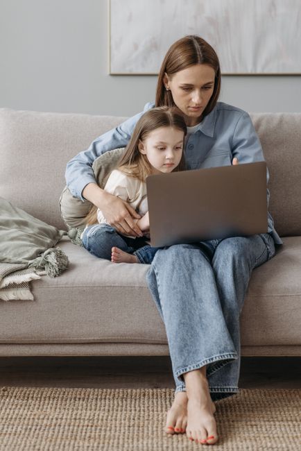 Mother and daughter sitting on sofa using laptop together, enjoying quality time indoors.