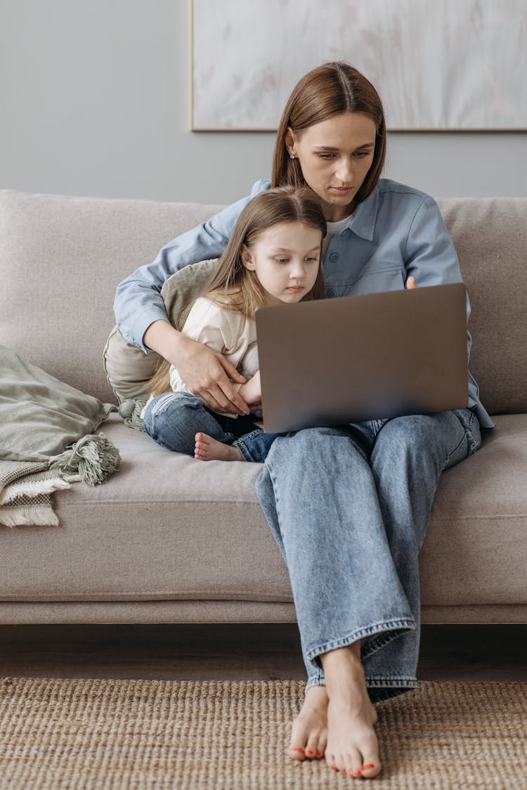 Mother And Daughter Sitting On The Couch Using A Laptop