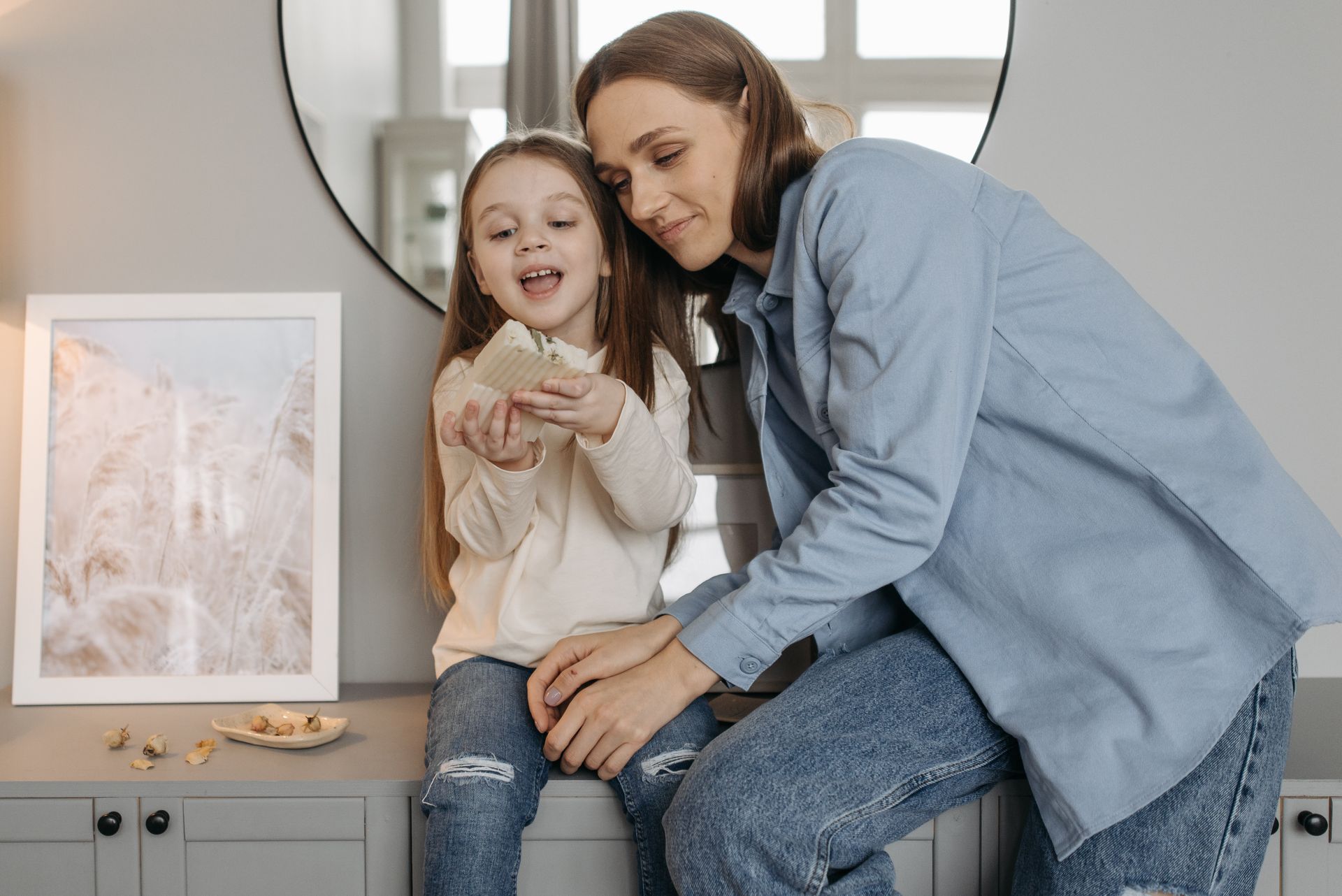 A mother and daughter share a moment of bonding indoors, engaging with a bar of soap.