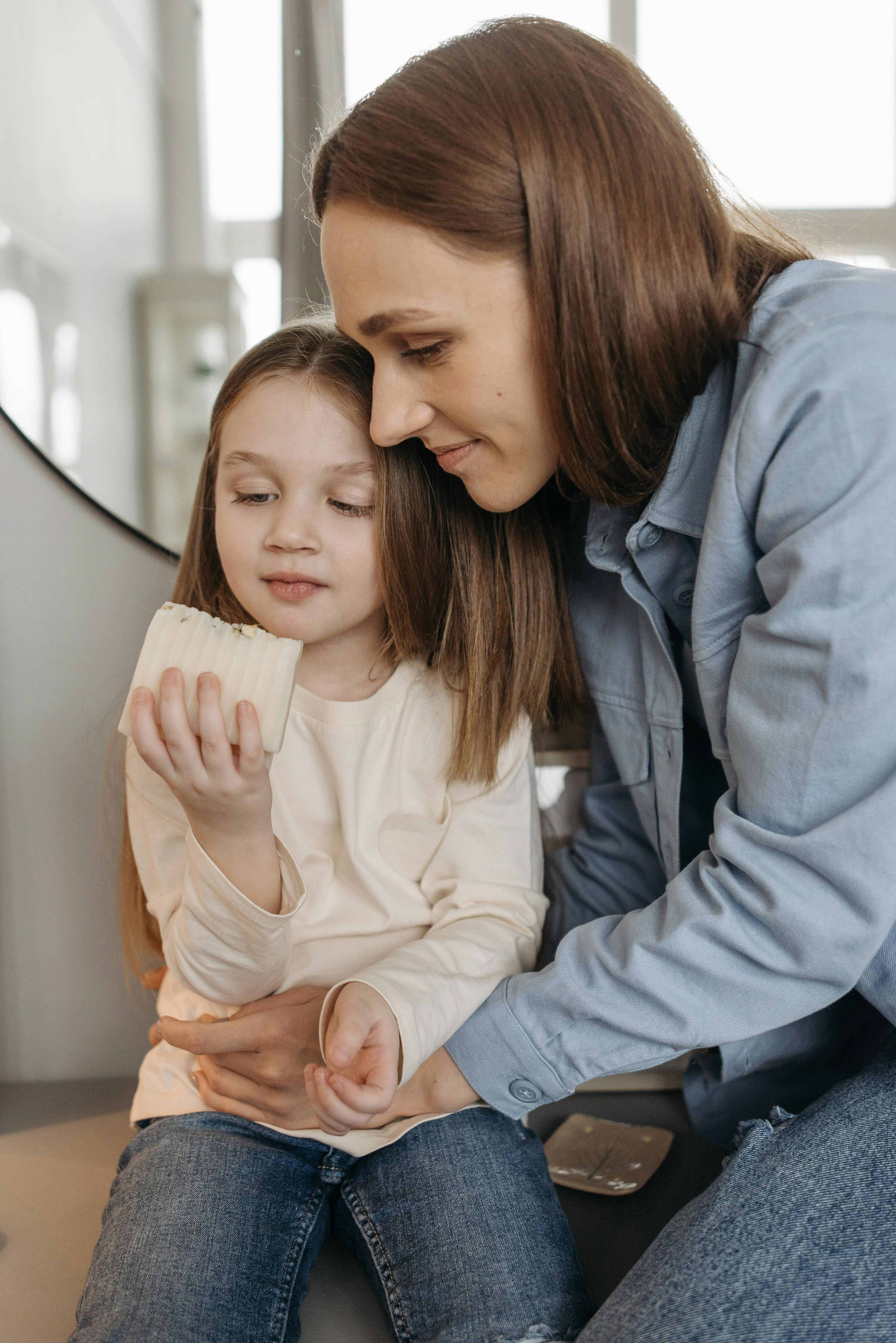 a woman and a child wearing long sleeves holding a bar of soap