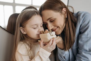 A Girl and a Woman Holding and Smelling Bars of Soap in a Ceramic Dish