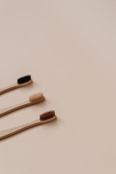 Three wooden toothbrushes with colorful bristles arranged on a beige surface, promoting sustainability.