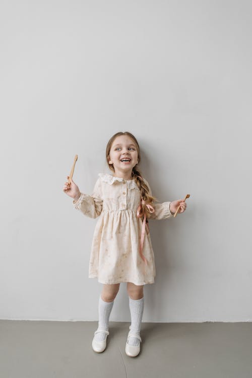 Girl in Long Sleeve Dress Holding Brown Wooden Toothbrushes
