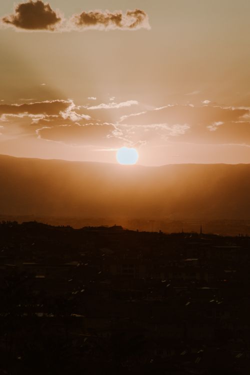 Free Silhouette of a town during a vibrant sunset behind mountains, casting a warm glow. Stock Photo
