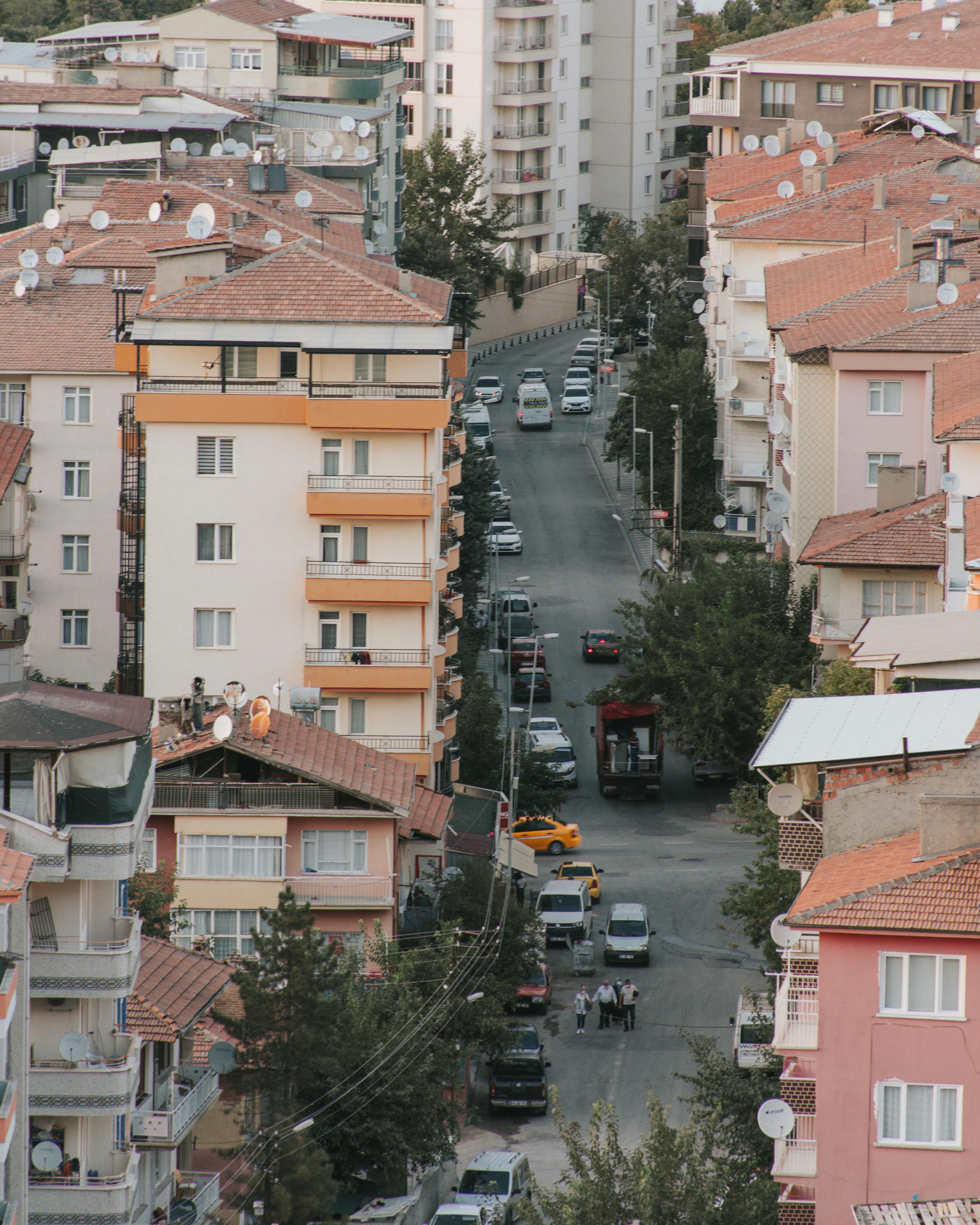 High angle shot of urban street surrounded by apartment buildings with cars and pedestrians.