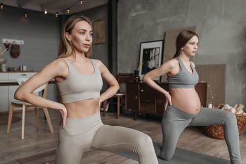 Free Two women, one pregnant, practicing yoga indoors wearing activewear. Stock Photo